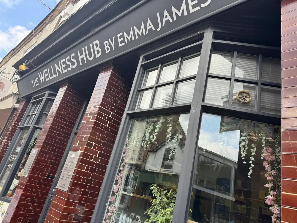 The exterior of The Wellness Hub by Emma James, featuring large windows with hanging decorations and a sign above the entrance.