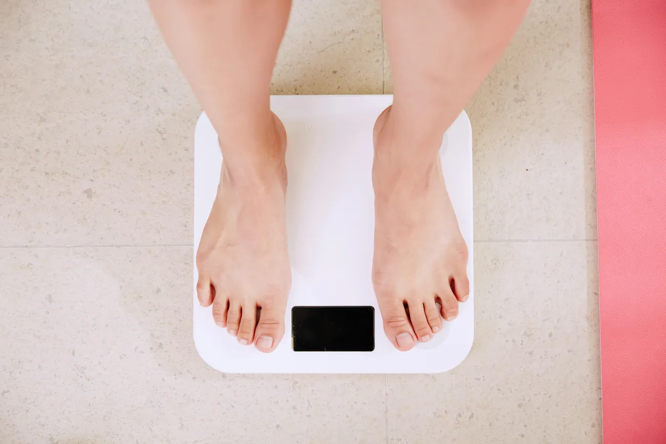 A person stands barefoot on a white digital bathroom scale placed on a light-coloured floor.