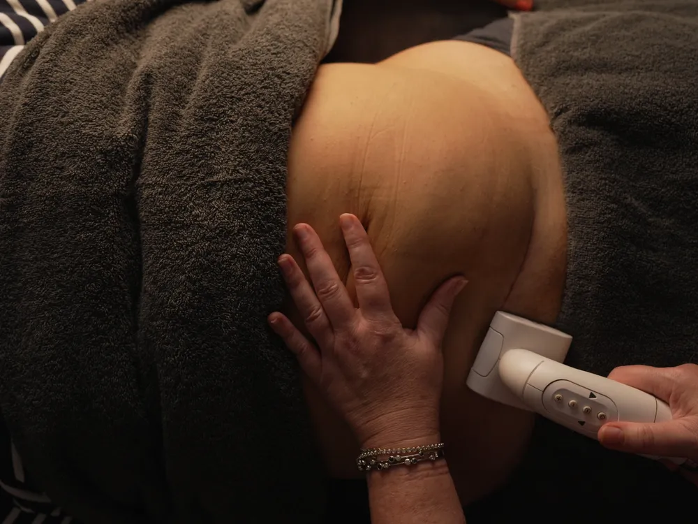 A person receives an ultrasound treatment on their abdomen while covered with a dark towel.