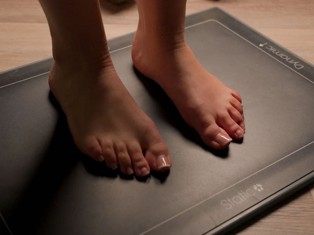 Close-up of two bare feet standing on a black electronic scale placed on a wooden floor.