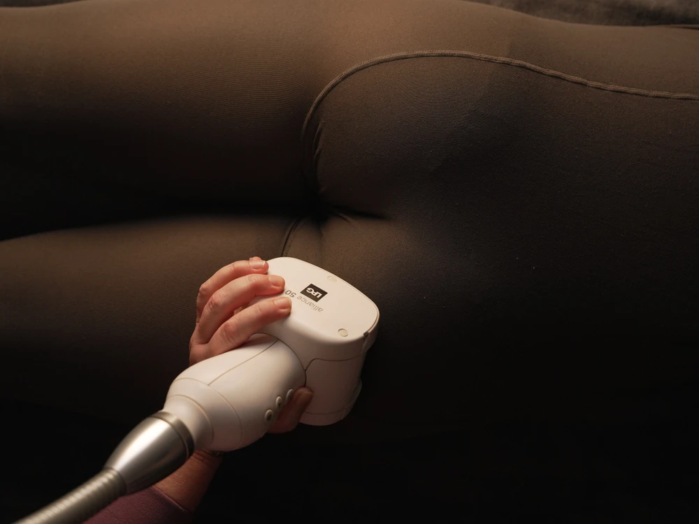 A person uses a handheld massage or therapy device on the thigh of someone wearing dark fitted clothing.