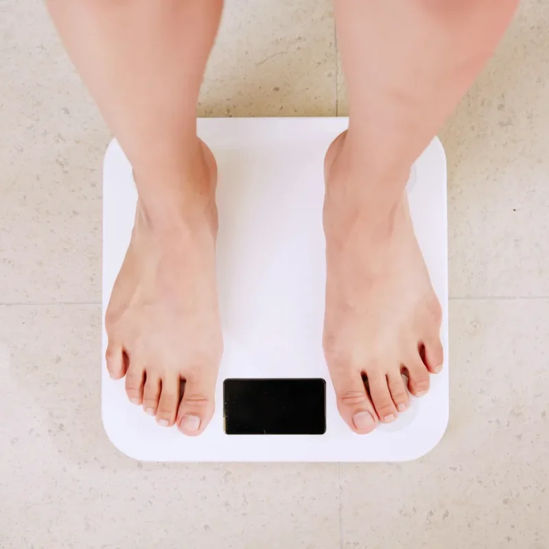 A person stands barefoot on a white digital bathroom scale placed on a light-coloured floor.
